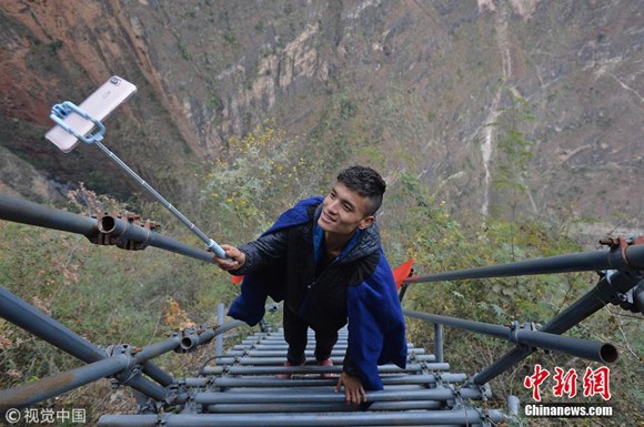 Yang Yang, an online celebrity, makes live streaming webcast with a selfie stick and introduces the scenery of the cliff village by climbing a steel structure stair on the cliff in Liangshan Yi Autonomous Prefecture, southwest China's Sichuan province, Dec. 15 2017.  (Photo/VCG)