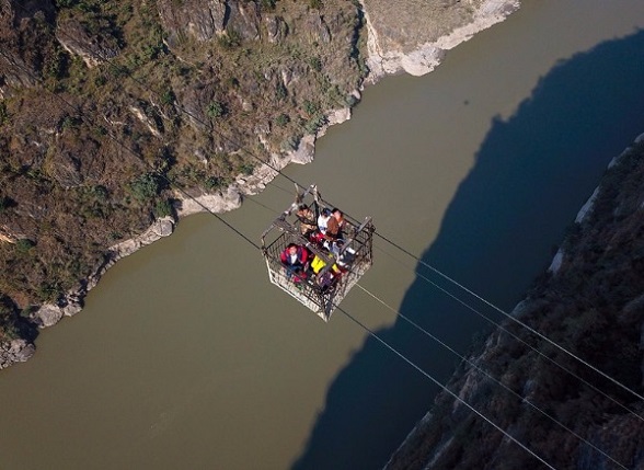Residents use an aerial cable bridge to cross the Jinsha River, a major tributary of the Yangtze River, in Butuo county, Sichuan province, on Friday. This is the last cable bridge in use across the river. A new bridge is expected to be put into use early next year. (Zhang Zhi/For China Daily)