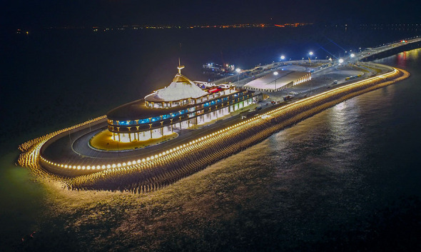 The east man-made island of the Hong Kong-Zhuhai-Macao Bridge is illuminated on Saturday. Cars exiting the bridge then enter a tunnel built into the island. (LIANG XU/XINHUA)