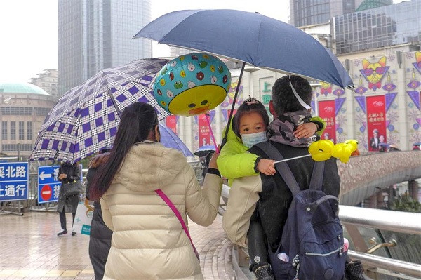 A pair of parents holding their child walk in the rain in downtown Xujiahui area on Sunday. The first cold snap of the winter is to hit the city from this morning, forecasters said. (Wang Rongjiang/SHINE)