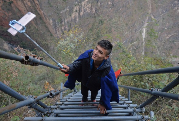 Yang Yang, of the Yi ethnic group, live-broadcasts climbing the steel ladder at Atuleer, a village in Zhaojue county, in the Liangshan Yi autonomous prefecture, in December. (Photo by Wang Qin/For China Daily)