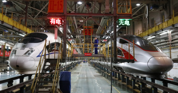 A Fuxing (rejuvenation) bullet train (right) and a Hexie (harmony) bullet train undergo maintenance at a depot late at night in Beijing earlier this month. (Photo by Zhu Xingxin/China Daily)