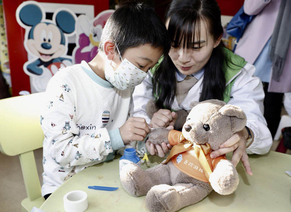 A young patient, accompanied by a social worker, learns to give an injection to a stuffed bear, as part of his play therapy, at the Children's Hospital of Fudan University in Shanghai. (Photo provided to China Daily)