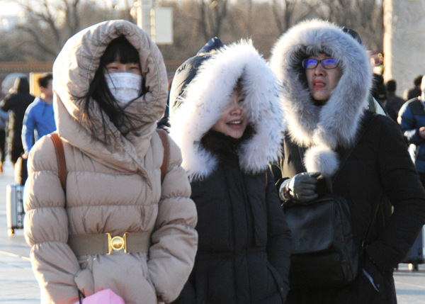 Tourists wear thick down jackets walking on Chang'an Street in Beijing. (Photo by Du Jia/For China Daily)