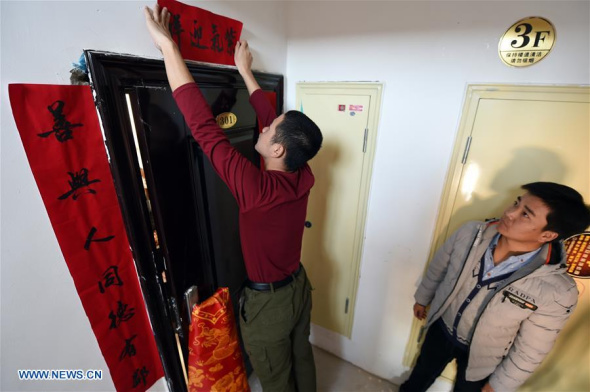 Xu Cun's son Huang Yubin (L) and a friend paste couplets at Xu's new apartment in a relocation community in Gulang, Northwest China's Gansu province, Feb 7, 2018. Xu Cun, with a disabled husband ill in bed and mother-in-law over 70, is the backbone of her family. Photo/Xinhua