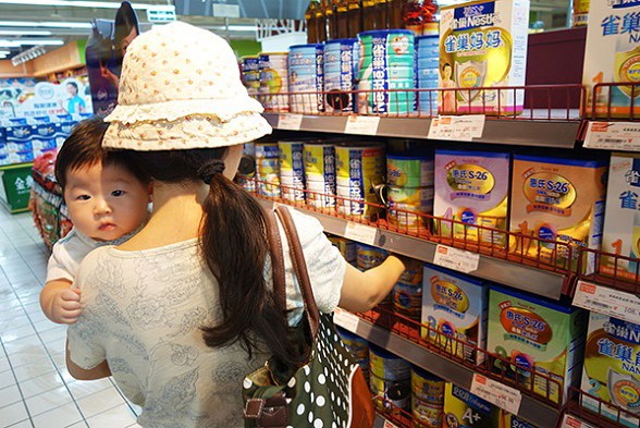A woman with a baby selects imported infant formula in a Beijing supermarket. (Photo/China Daily)