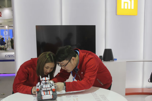 Two technicians fine-tune a robot at the stall of Xiaomi Corp at an industry expo held in Wuhan, Hubei province. (Photo by Chu Lin/ For China Daily)