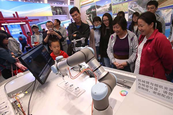 Visitors watch an intelligent mechanical device equipped with 5G technology in operation during an exhibition in Beijing. (Photo by Chen Xiaogen/for China Daily)