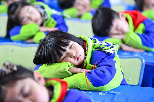 Elementary school students practice a healthy position for napping in Bozhou, Anhui province, on Wednesday, which was World Sleep Day.(Photo by Liu Qinli/for China Daily)