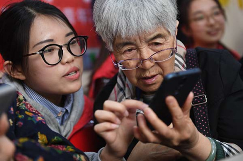 A volunteer teaches an elderly woman how to use a smartphone in Taiyuan, Shanxi Province, on Tuesday. (Photo by Wu Junjie/China News Service)