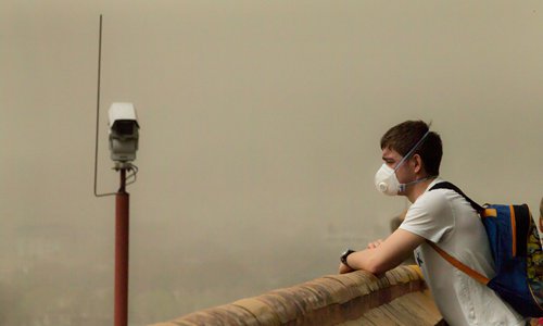 A foreigner wearing a mask stands in a pavilion in Beijing's Jingshan Park on Wednesday. The pavilion, which provides the best view of the Forbidden City, suffered from low visibility as a sandstorm hit Beijing after days of heavy smog. (Photo: Li Hao/GT)