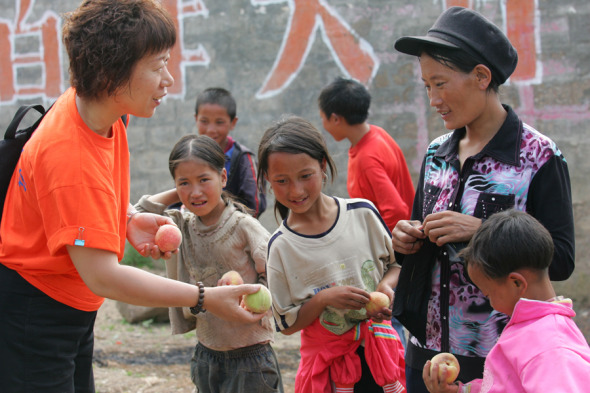 Zhang Junlan gives peaches to children at a village in Liangshan, Sichuan province, during one of her many trips to the remote area. (Photo/China Daily)