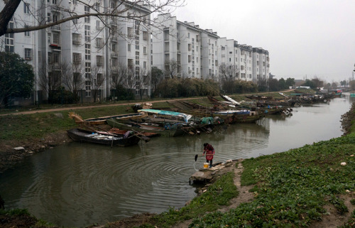 A villager washes a mop in the river in Xiaomei village, Wuxing district, Huzhou, opposite a building in which former fishermen have been resettled. (GAO ERQIANG/CHINA DAILY)