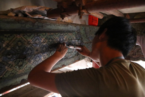 A staff member of the renovation project of Baoyun Lou, or the Hall of Embodied Treasures, fixes a painting on a piece of wood. (PHOTO BY WU WEI/FOR CHINA DAILY)