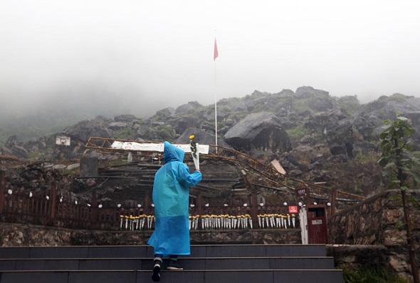 A man lays flowers on Tuesday at the site of Maoba Middle School, which was destroyed in the 2008 earthquake. Many bodies still lie beneath the rubble. (Zou Hong/China Daily)