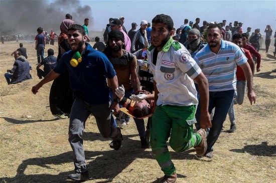 Palestinian medics and protesters carry an injured man during clashes with Israeli troops near the Gaza-Israel border, east of Gaza City, on May 14, 2018. (Xinhua/Wissam Nassar)