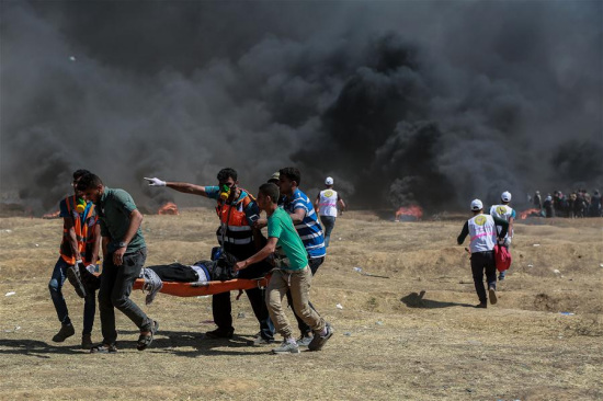 Palestinian medics and protesters carry an injured man during clashes with Israeli troops near the Gaza-Israel border, east of Gaza City, on May 14, 2018. (Xinhua/Wissam Nassar)