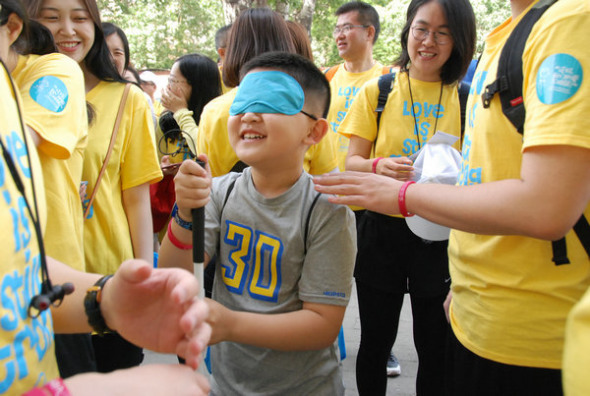 A boy at the Wishbone Day event walk with his eyes covered to experience OI which may affect eyesight in some cases. (Photo provided to China Daily)
