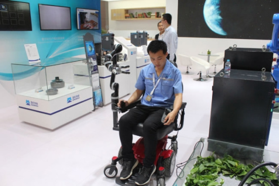 A staff member demonstrates how to operate an intelligent wheelchair with a robotic arm. The wheelchair can be operated by pressing buttons and moving a handle. It can move and fetch things for patients. /China Plus Photo