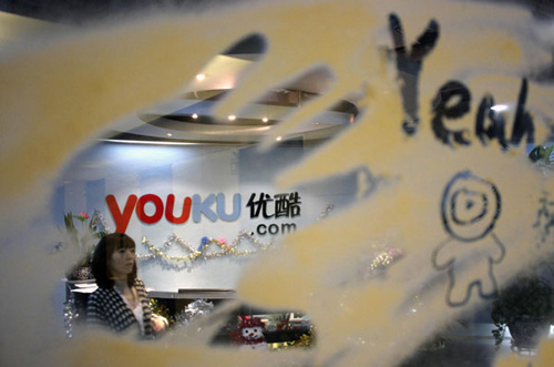 An employee is seen through a glass wall as she walks past the logo of Youku.com above the reception desk at the company's headquarters in Beijing, in this Dec 9, 2010 file photo. [Photo/Agencies]