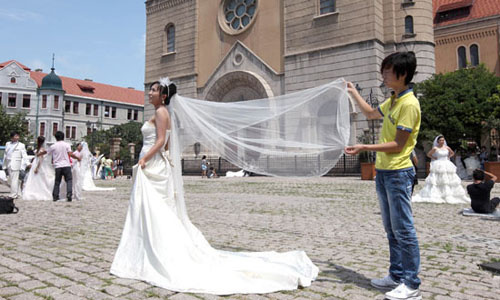 Wedding couples take pictures in front of a Catholic church in Qingdao, Shandong province. Couples in Shanghai spend an average of 4,127 yuan ($653) on their wedding photos. [Photo / Agencies] 