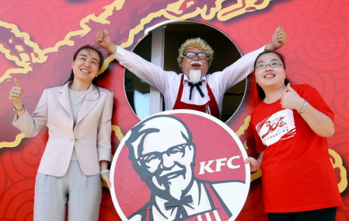 Two customers pose with a staff member dressed as the mascot of Kentucky Fried Chicken, Colonel Sanders, for photos at the opening ceremony of the 300th restaurant in Beijing. Yum! Brands Inc, the Louisville, Kentucky-based company, which owns both KFC and Pizza Hut, has over 3,800 KFC restaurants on the Chinese mainland 25 years after it entered the market. [Photo/Xinhua]