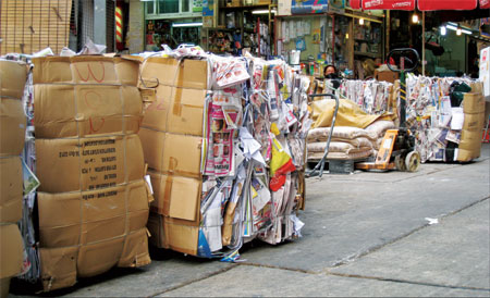 Tons of compressed waste newspapers and cardboards collected by peddlers pile up outside a Wan Chai environmental shop to be transported to a collection center. [Photo / China Daily] 