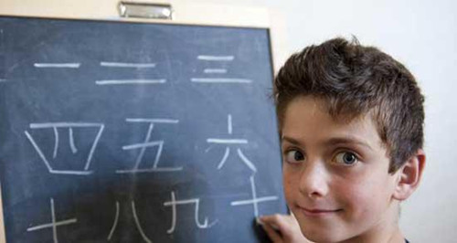 Young western boy writing mandarin Chinese on blackboard.