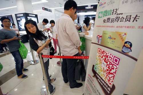Customers stand next to a poster advertising the WeChat instant messaging service at a shopping mall in Shanghai. Tencent Inc, the provider of WeChat, said the service now has more than 300 million users. [Photo / China Daily]