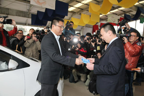Qian Jun (right), a 38-year-old office clerk in Shanghai, receives the license plate to his Roewe E50, the first domestically produced electric vehicle, on Wednesday. [Photo/China Daily]