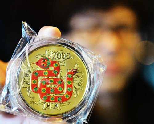 A gold jewellery shop staff member demonstrates a gold coin issued by the People's Bank of China in Hangzhou, capital of east China's Zhejiang Province, Feb. 7, 2013. In 2012, consumers in China bought a total of 832.18 tons of gold, 71.13 tons, or 9.35 percent, more than the figure of 2011, according to the latest statistics released by the China Gold Association on Saturday. (Xinhua)