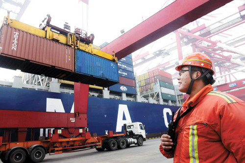 A worker looks on as containers are offloaded in Qingdao Port, Shandong province. Chinas imports declined 15.2 percent year-on-year in February because of weaker internal demand. [Yu Fangping/for China Daily]