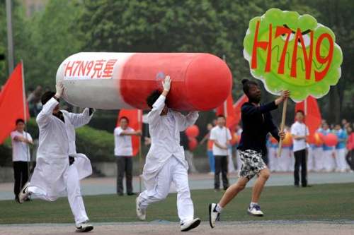 Two college students carrying a model of a capsule chase another student holding a banner reading H7N9 during a performance at the opening ceremony of the sports meeting hosted by Chongqing University in Southwest China's Chongqing municipality on Friday. The characters on the capsule model read H7N9 killer.(CNS/CHEN CHAO)