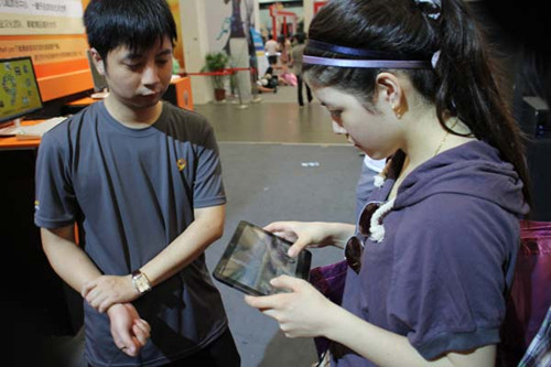 A woman playing an online game on a tablet PC as a man watches. Game developers and distributors in China are searching for ways to attract more people to download gaming apps after estimates that the turnover of the mobile gaming market could hit 20 billion yuan ($3.2 billion) by 2015. Provided to China Daily