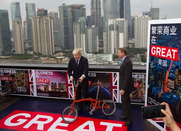 Mayor of London Boris Johnson (left) poses with a fold-up bicyle on a 30th-floor balcony overlooking the Bund in Shanghai on Wednesday. Johnson came to China to promote trade, investment and products from Britain. Gao Erqiang / China Daily