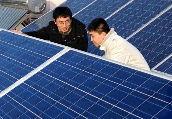 Xu Pengfei (L), China's first individual user of grid-connected photovoltaic (PV) power, introduces PV solar batteries to his friend on the top of his flat building in Qingdao, east China's Shandong Province, Jan. 13, 2013.   