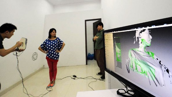 A member of staffs scans a young couple to make 3D-printed figurines at a newly-opened 3D printing gallery in Chongqing, Southwest China's municipality, June 3, 2013. [Photo/Xinhua]