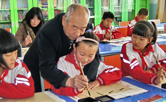 Chen Guokun, 72, teaches a student how to use a calligraphy brush at a primary school in Hohhot, the Inner Mongolia autonomous region, in March. Chen is a retired teacher but has volunteered at the school for more than a year.[Photo / Xinhua]