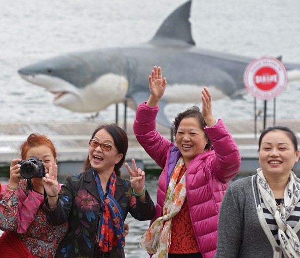 Chinese tourists pose for photographs in front of a 7.4-meter-long great white shark replica in Sydney Harbour in November. Chinese overtook US citizens as the world's biggest-spending travelers in 2012. Greg Wood / for China Daily  