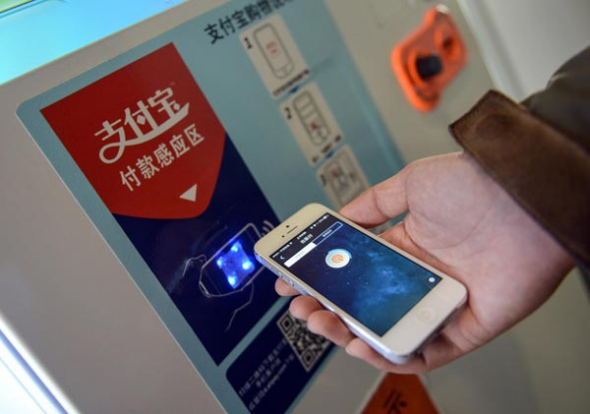 An employee at Alipay, the online payment arm of Alibaba Holding Group Co Ltd, shows how to make payments by scanning a bar code with mobile devices in Hangzhou, Zhejiang province. China's central bank ordered on Friday a halt to such payments amid concerns over the security of their verification procedures. Han Chuanhao / Xinhua