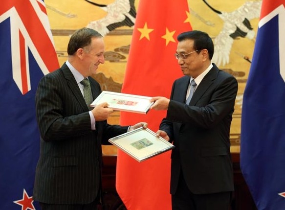 Premier Li Keqiang (R) and New Zealand Prime Minister John Key exchange sample banknotes at a ceremony in the Great Hall of the People in Beijing on Tuesday. They announced that the two countries have approved direct trading between their currencies. Photo by Wu Zhiyi / China Daily