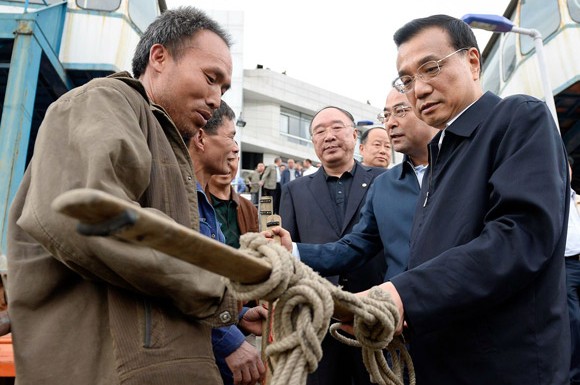 Premier Li Keqiang examines the pole of a bangbang, a traditional porter who helps residents carry bags, at Wanzhou port in Chongqing on Sunday. [Photo / China News Service] 