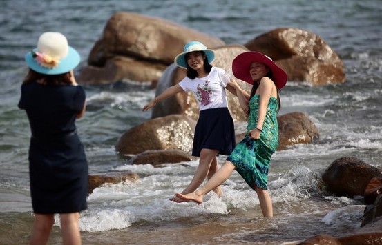 Tourists pose for pictures in Sanya, Hainan province, May 3, 2014. Residents of South China's Sanya city, Hainan province, are set to each get 360 yuan ($57.6) as subsidy as the local government began granting half-year funds on Monday to offset rising prices. [Photo / Xinhua]   