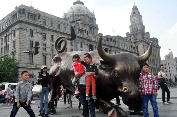Tourists pose beside the bronze statue of a charging bull on the Bund in Shanghai early this month. [Photo by Yan Daming / For China Daily]  