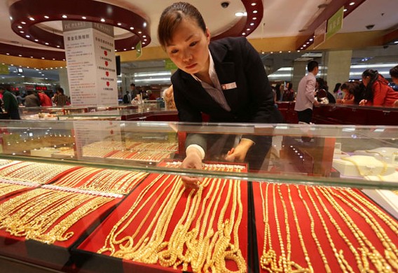 An assistant arranges jewelry items at a gold shop in Xuchang, Henan province. China's gold demand fell 18 percent in the first quarter of this year, the World Gold Council said. GENG GUOQING/CHINA DAILY  