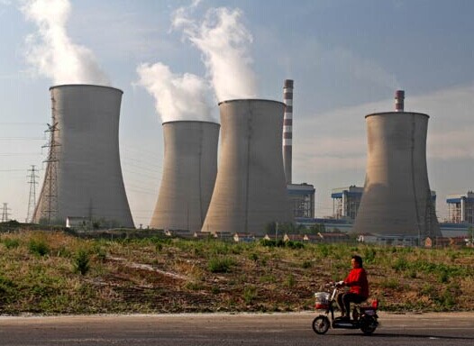 A woman passes a thermal power plant of China Huaneng Group Corp in Huai'an, Jiangsu province. By the end of this year, all coal-fired power plants of the group will be equipped with desulfurization and dust removal equipment. CHINA DAILY  