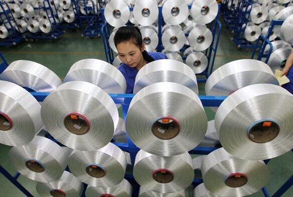 A worker inspects rolls of polyester fiber at a factory in Nantong, Jiangsu province. [Photo/China Daily]  