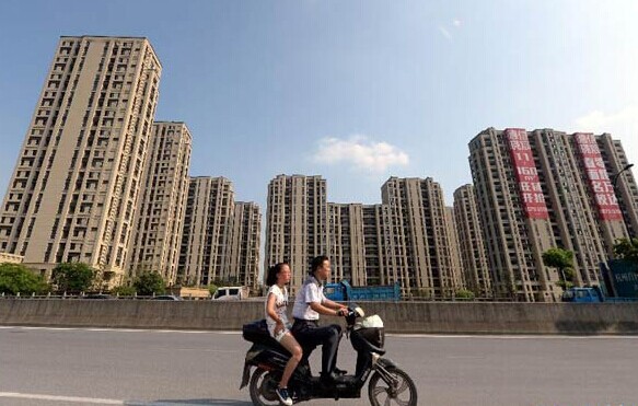 Riders pass by newly-built apartments in Hangzhou, capital of East China's Zhejiang province, July 29, 2014. [Photo/Xinhua]  