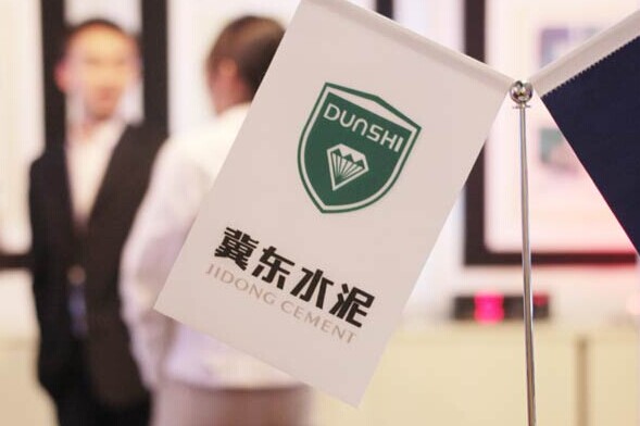 The Tangshan Jidong Cement Co logo is displayed at a recent construction materials exposition in Beijing. Three cement companies, including Tangshan Jidong, were fined for manipulating cement prices and reaching price-fixing agreements.CHINA DAILY