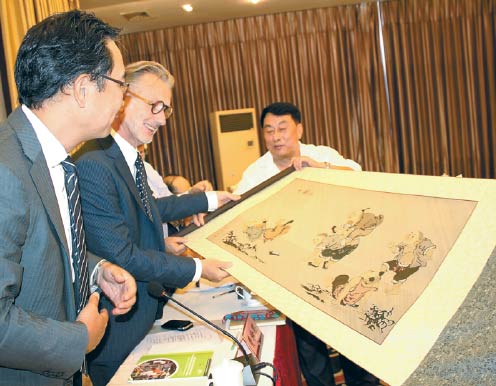 Hans Friederich (center), director general of the International Network for Bamboo and Rattan, appreciates a traditional Chinese painting made of bamboo in Yibin, Sichuan province, earlier this month. The producer of the painting has benefited from the China Sustainable Bamboo Enterprise Program. HUANG ZHILING/CHINA DAILY  